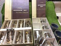 Two sets of brown glass beverage glasses in original boxes, one box missing a glass, showing retro geometric black and gold patterning.