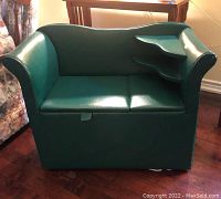 Front view of the vintage green settee showing seat cushions and shape. Storage compartment tab visible under seat.
