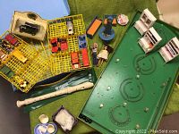 Yellow plastic Dinky car case with multiple vintage toy cars inside, two dolls, toy flute, dollhouse furniture and small accessories on a blue surface.