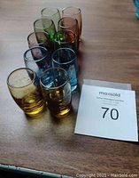 Ten assorted colored shot glasses arranged closely together on a wooden surface.