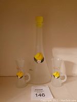 Set of one large bottle and two small glasses with handles featuring Baci branding and yellow lemon decal.