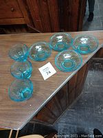 Seven blue glass cups and bowls displayed on a wooden surface: three cups on the left, four bowls on the right.