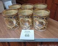 Photo showing six cylindrical glasses with cheetah print and gold accents arranged on a surface.