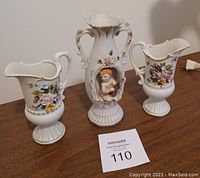 Three porcelain vases on wooden surface showing floral and angel decorative features