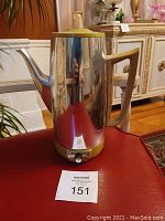 Full side view of the coffee maker showing the stainless steel body, plastic handle and lid, and general shape.