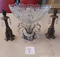 Image of a table display featuring one glass bowl with intricate cut patterns and two ornate metal candle stick holders with hanging glass crystals.