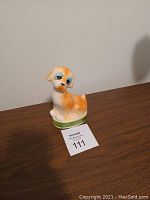 Glass dog figurine sitting on a wooden surface with light orange and white coloring and blue eyes, photographed to show condition and details of the figure.