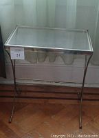 Full view of a rectangular glass table with a metal frame, placed on a wooden floor with a light-colored curtain background.