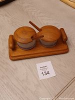 Top-down view of the wooden tray holding two glass cups with wooden lids and wooden spoons inside.