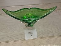 Green translucent decorative glass bowl with pointed ends, photographed on a wooden surface with lot number 1 tag below it.