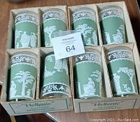 Photo showing eight Hellenic glassware glasses in two boxes, each glass featuring white classical Greek imagery on a translucent green background, boxed and arranged in two sets of four.