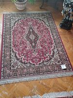 Full view of a decorative rectangular rug on wooden parquet floor with floral and medallion design in red and black tones.