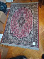 Full view of rectangular living room rug with red background, floral medallion, and fringed edges.