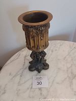 Metal antique-style candle holder with ornate details stands on a marble surface with a lot number card in front.