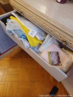 Drawer with assorted folded tablecloths in various colors including white, blue, yellow, and beige tones, some in packaging.