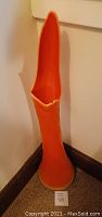 Tall orange ceramic umbrella stand with scalloped rim photographed against a white wall