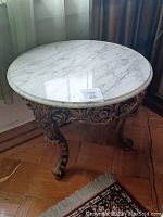 Round marble top side table with ornate carved wooden base shown near window