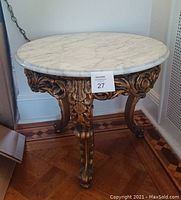 Photo of round marble table showing white marble top and ornate carved wooden base with three legs