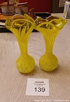 Two yellow decorative glass vases with ruffled tops and bulbous bases on a table.