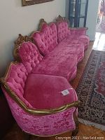 Side angle view of vintage pink velvet tufted couch showing gold carved wood frame and curved design.