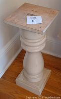 Full view of white wooden pedestal stand with square top and rounded column base.