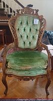 Full front view of antique chair showing carved wood and green tufted cushion