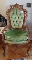 Full view of the wooden antique chair with green velvet button-tufted backrest and seat cushion.
