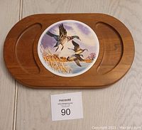 Wooden cheese platter shaped like a tree with three cutout compartments and a ceramic plate with flying ducks artwork placed in the middle cutout.