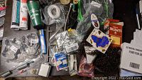 Overhead view of assorted lot items spread on surface including various packaged and unpackaged items such as tubes, hardware, and sealed goods.