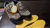 Pair of brown and grey Tiger safety steel toe work shoes with black reinforced toe caps displayed with yellow insoles laid in front on a dark table.