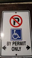 Full view of the white metal sign showing no parking symbol, wheelchair symbol, and text 'BY PERMIT ONLY' with directional arrows.