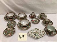 Multiple Rose Medallion pieces arranged: deep cups on saucers, small cups on saucers, bread plates and oval dish