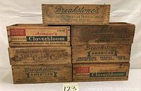 Seven antique wooden dovetail cheese boxes with different brands and logos arranged to show front and side panels.
