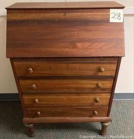 Front view of the antique slant front desk showing the fold-down slant top and three drawers with wooden knobs.