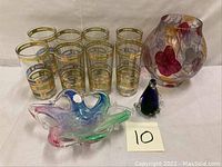 Photo showing set of eight gold gilt glasses, Murano glass dish, penguin paperweight, and floral vase arranged together.