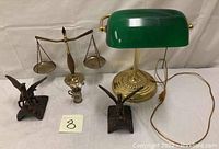 Photo showing emerald green bankers lamp, brass balance scale with two pans, and two bronze Pegasus horse figurines