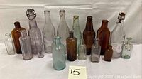 Full lot of 15 assorted antique and vintage collectible glass bottles in various sizes, colors, and shapes.