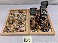Two wooden trays filled with assorted costume jewelry pieces including brooches, earrings, necklaces, and wristwatches.