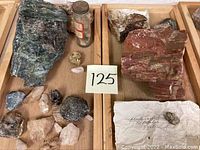 Overview of mineral rock collection in wooden trays showing variety and sizes of specimens including jar and label.