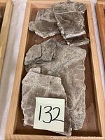 Photo showing multiple sheet-like mica mineral rocks with layered, flaky crystalline structure on wooden tray.