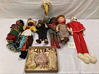 Wide view of the collection showing assorted dolls in various styles including stuffed cloth dolls, vintage porcelain dolls, large vinyl doll in red costume, and large bird plush doll.