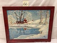 Frontal shot of the oil painting showing a winter countryside scene with a red house, trees, snow, and pond in a reddish wooden frame.
