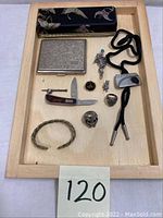 Photo of entire lot laid out on wooden tray showing pocket knife, cigarette case, rings, bolo tie, brooch, bracelet, and wallet.