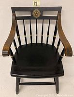 Front view of the Windsor arm chair with black painted seat, natural wood arms, and Harvard emblem on the backrest.