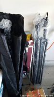Two tripod stands folded and wrapped in plastic next to a black fabric carrying bag containing crossbar sections.