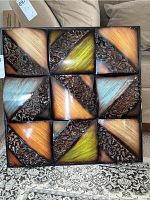 Front view of square metal wall art showing 9 decorative tiles with brown, green, orange, and teal colors and leaf scroll textures.