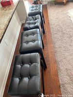 Four black faux leather cushioned barstools arranged in a row parallel to a counter