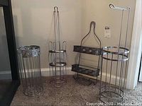 Photo showing four metal bathroom accessories: three toilet paper holders and one two-tier hanging shower caddy, arranged on carpet near wall.