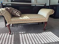 Front side view of gold upholstered bench with cherry wood legs showing rolled arms and patterned fabric.