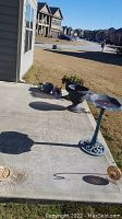 Concrete patio with birdbath, large planters, blue ceramic pots, and shepherd hook arranged with lawn background